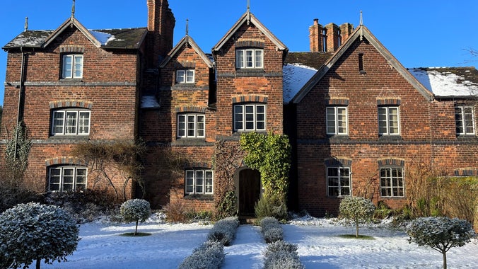 The front of Moseley Old Hall in the winter sun. The sky is a deep blue and the grass infront of the house is covered with morning frost